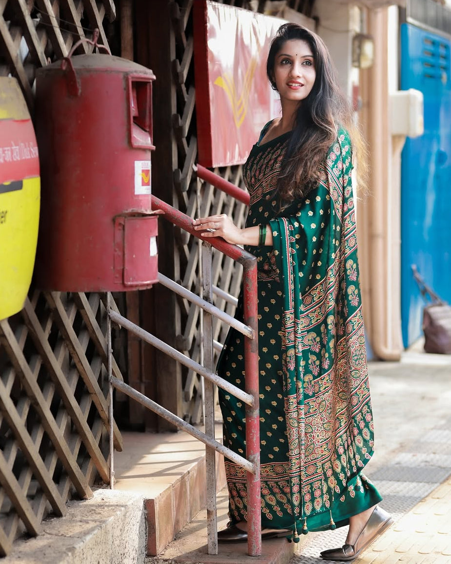 Woman in a green saree standing next to a red mailbox on a street.